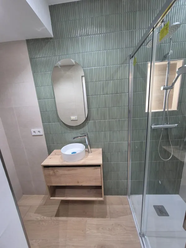 Alicatado de baño en verde con lavabo de madera y mampara de cristal