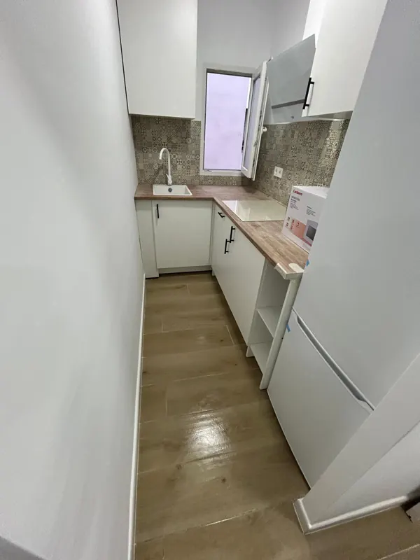Cocina pequeña reformada con muebles blancos, encimera de madera y suelo laminado