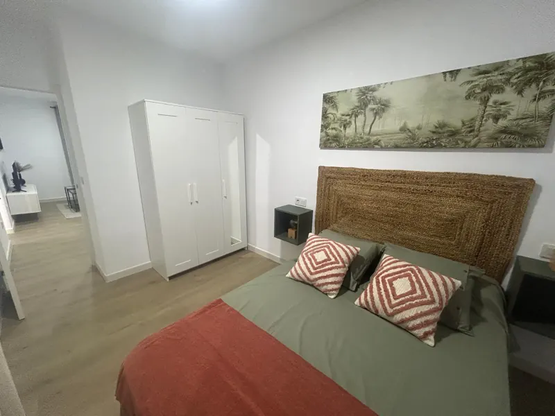 Dormitorio reformado con suelo laminado, cabecero de fibra y ropa de cama verde y teja