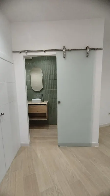Puerta corredera de cristal con guía vista de acero en la entrada de un baño reformado